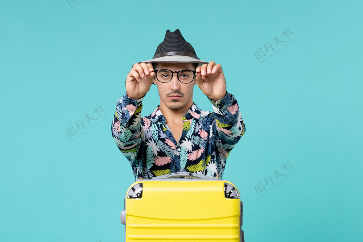 假期年轻男子正拿着他的黄色袋子准备在蓝色的墙上旅行成人旅行人