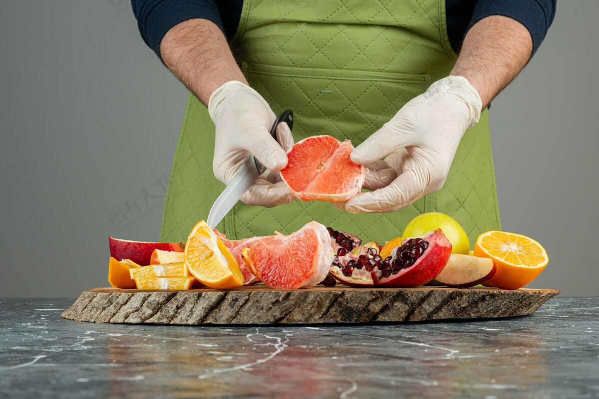 混合男性手戴手套在大理石桌上切多汁的葡萄柚切石榴橙子
