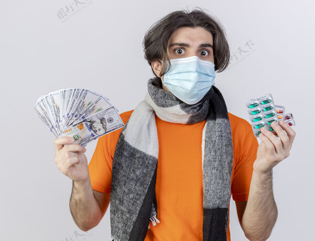 面具年轻的病夫戴着围巾和医用口罩拿着药片和现金隔离在白色的男人持有穿