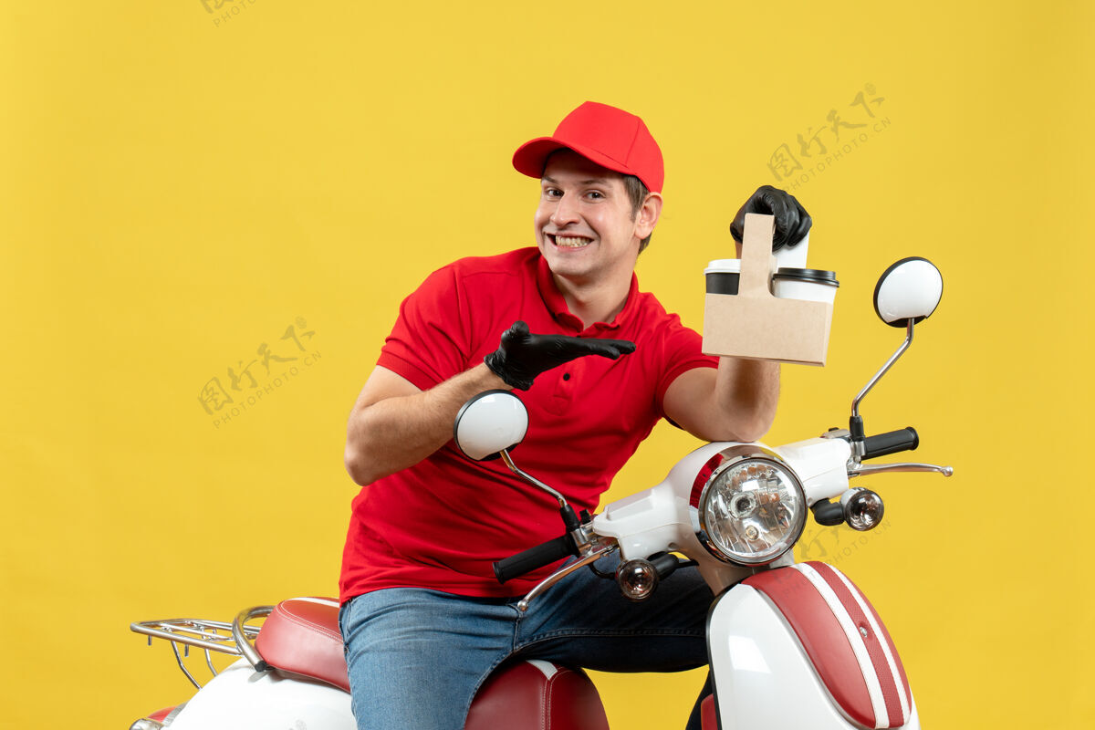 车辆正面图微笑的快乐快递员身穿红色上衣 戴着帽子手套 戴着医用口罩 坐在滑板车上点菜交付前面坐着