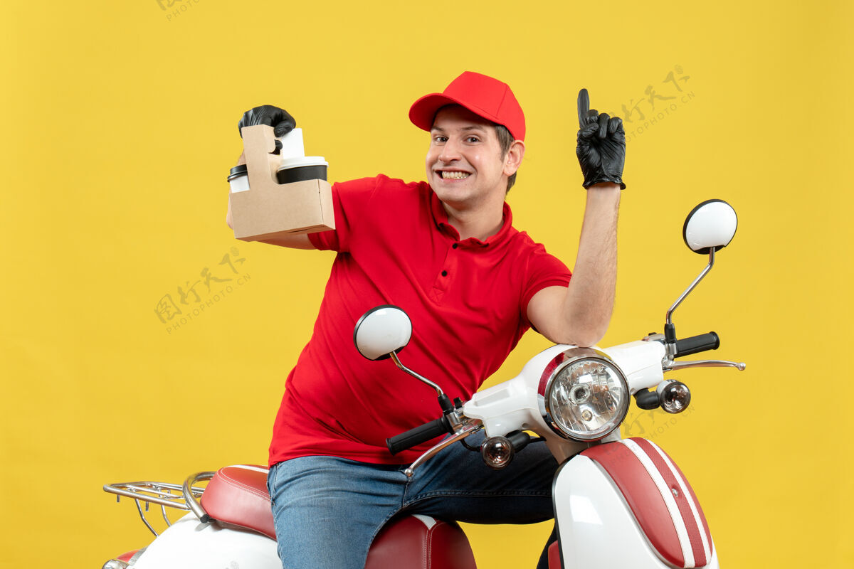 车辆正面图微笑的快递员身穿红色上衣 戴着帽子手套 戴着医用口罩 坐在滑板车上 拿着订单 指着上面运动摩托车前面