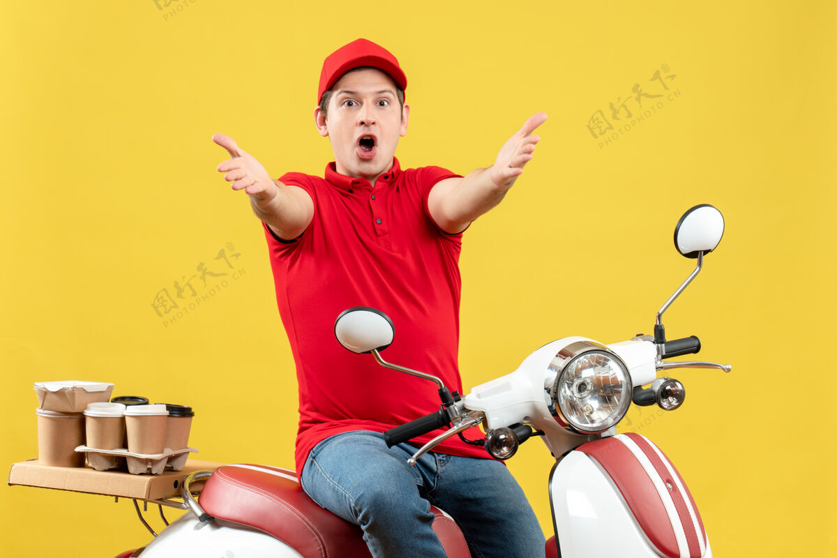 成人前视图震惊的年轻人穿着红色上衣和帽子传递命令 伸出他的手臂向前黄色背景红色交付手臂
