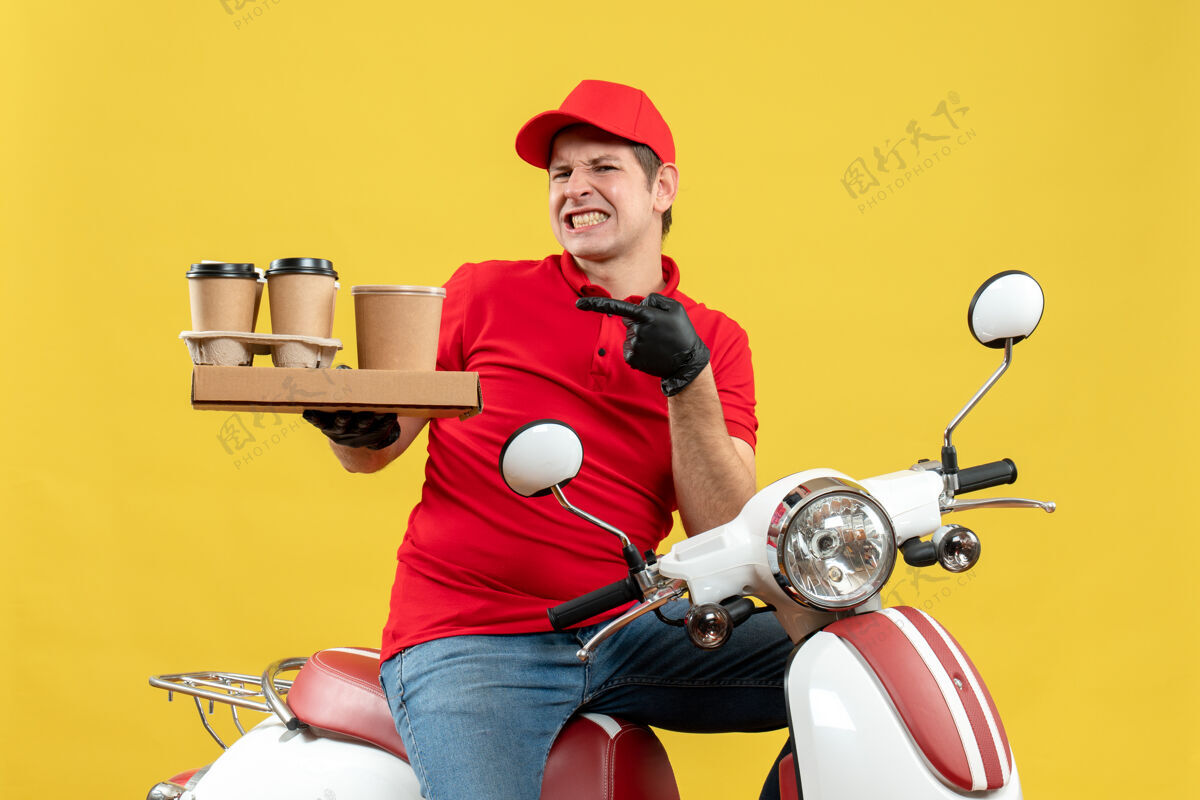 面罩前视图情绪紧张的快递员身穿红色上衣 戴着帽子手套 戴着医用面罩 坐在滑板车上拿着订单手套情绪摩托车