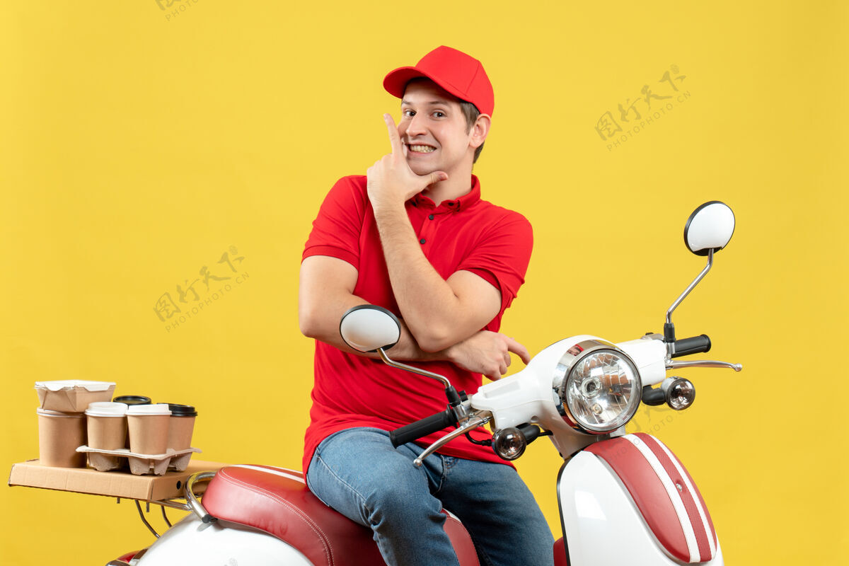 摩托车正面是一个自信快乐的年轻人 穿着红色上衣 戴着帽子 在黄色背景下传递着命令前面年轻人车辆