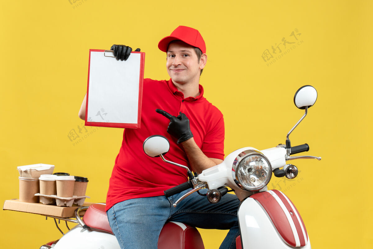 车辆正面图自信的快递员身穿红色上衣 戴着帽子手套 戴着医用面罩 坐在摩托车上拿着文件 传递着订单手套坐着命令