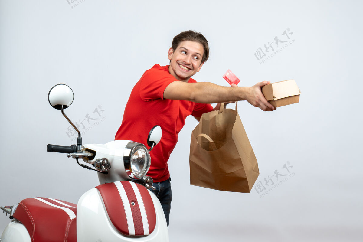 运动忙碌的送货员穿着红色制服站在滑板车旁 拿着白色背景上的银行卡订单人背景银行