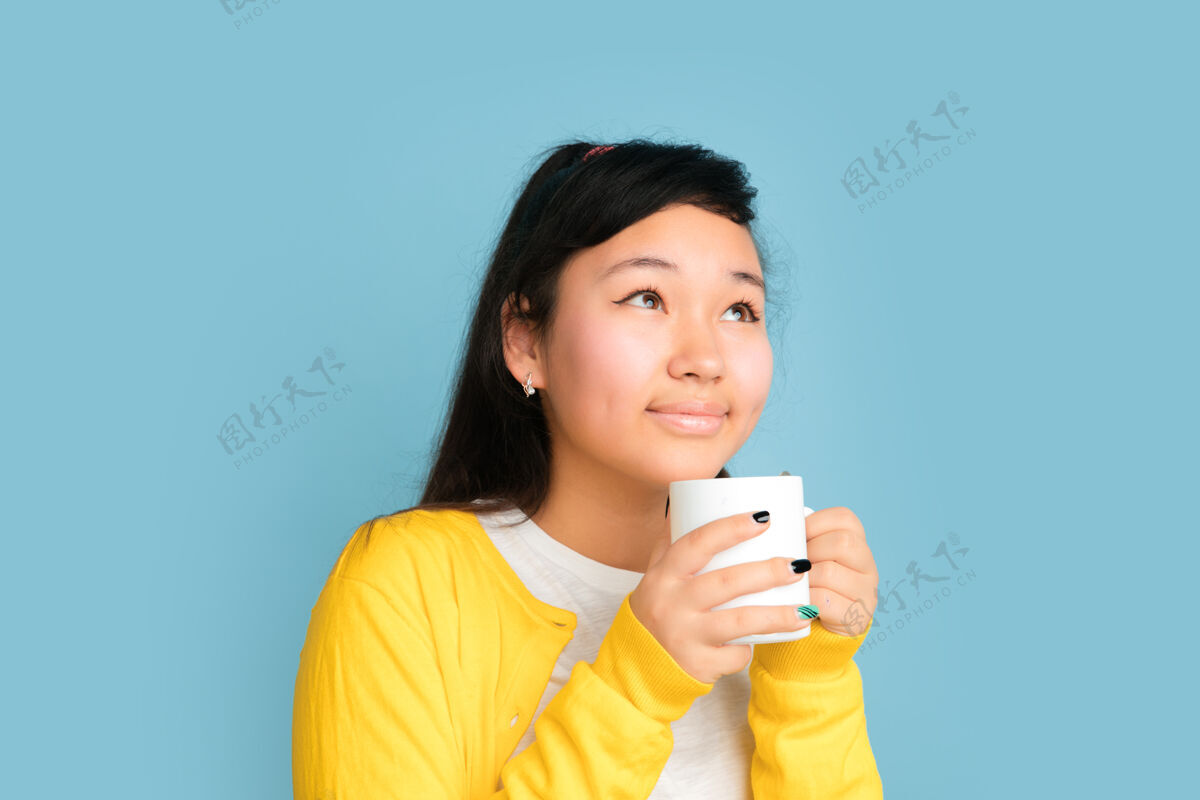 人以蓝色工作室为背景的亚洲青少年肖像美丽的深褐色长发模特人类情感的概念 面部表情 销售 广告喝咖啡或茶面部成功财务
