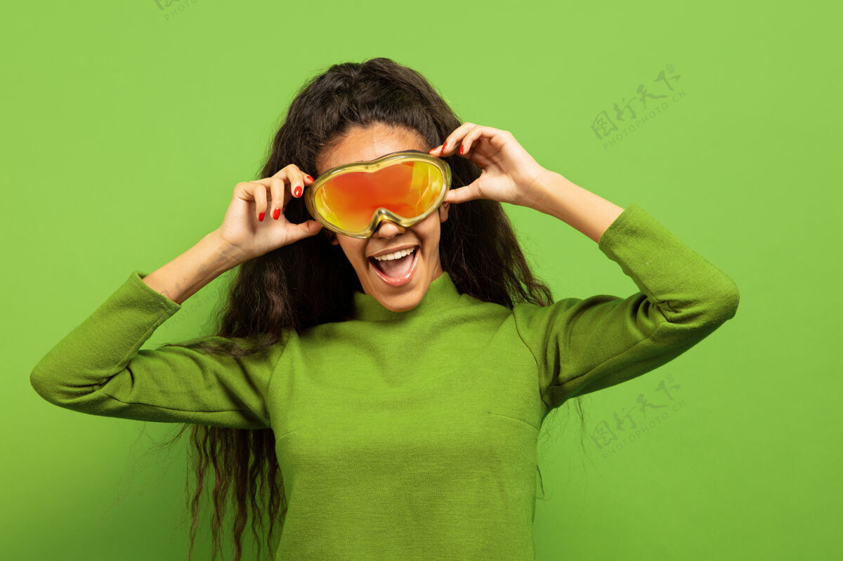头发以绿色工作室为背景 黑色皮肤的非洲裔年轻女子的滑雪面具肖像人类情感的概念 面部表情 销售 广告 冬季运动和假日微笑 戴眼镜滑雪人惊喜