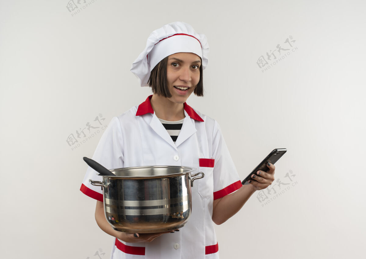 人面带微笑的年轻女厨师身着厨师制服 拿着锅和手机孤立在白墙上表情烹饪姿势