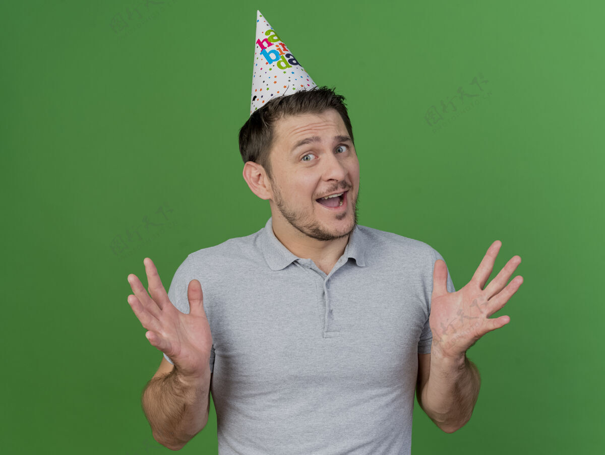 小伙子快乐的年轻人戴着生日帽摊开双手孤立在绿色派对帽子传播欢乐