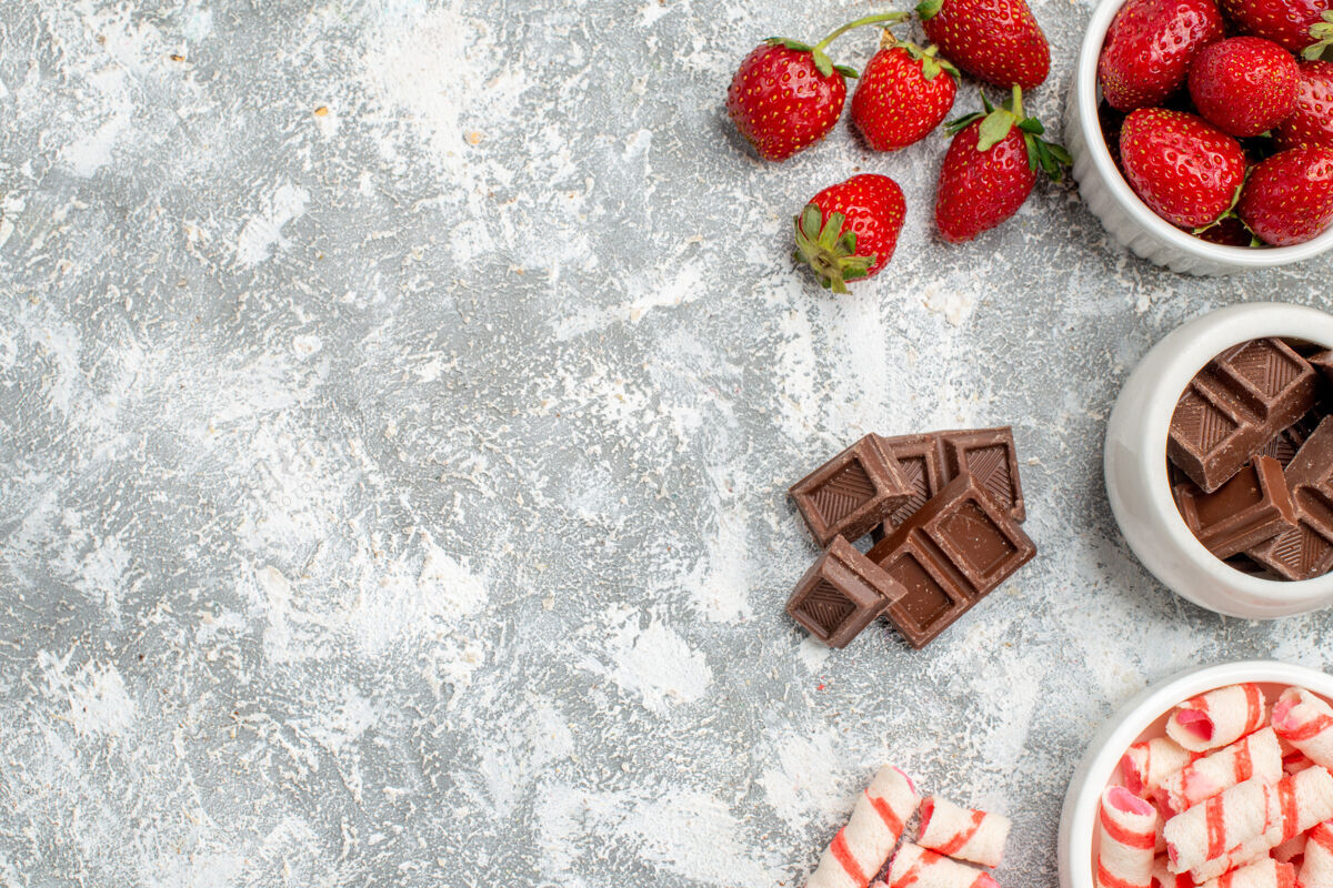 甜点在灰白色地面的右侧 有草莓巧克力糖果和一些草莓巧克力糖果的顶视图碗权利食物草莓