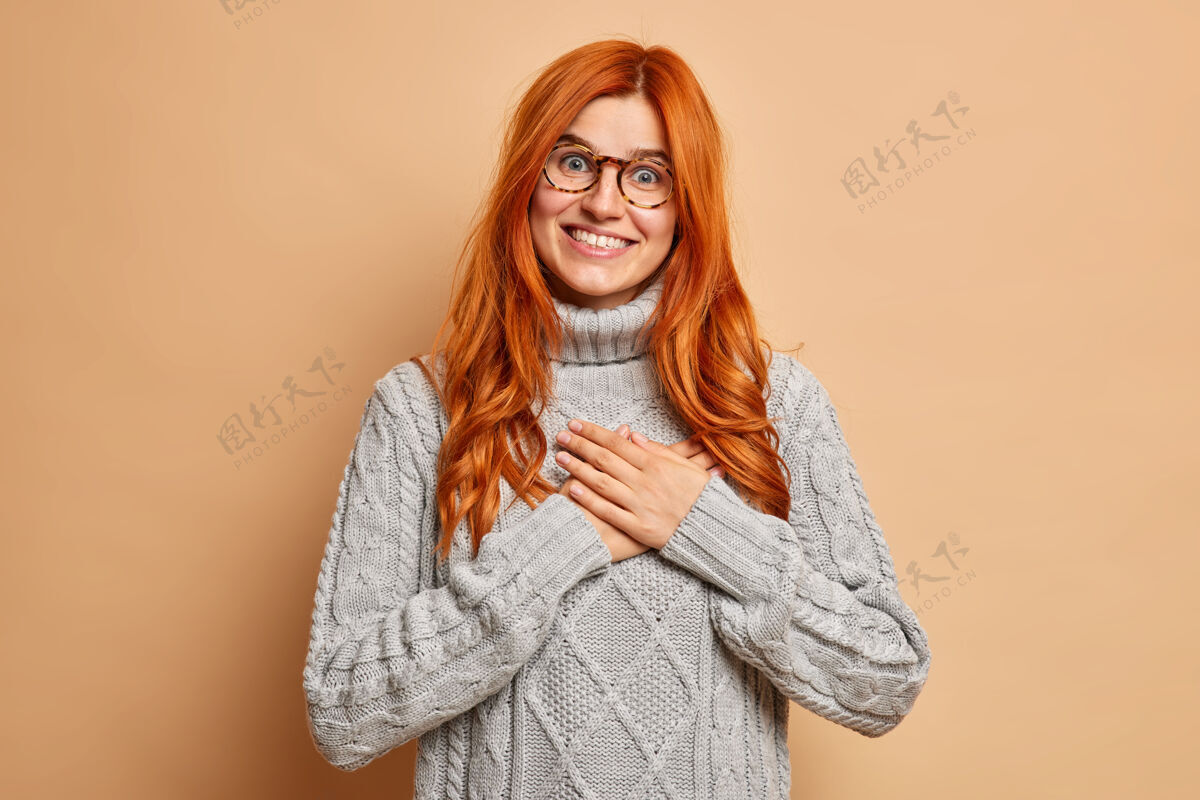 请快乐的红发女人双手贴在胸前做感恩的手势微笑着快乐地穿上针织的灰色毛衣人快乐肖像