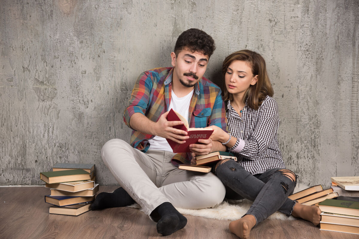 举行可爱的夫妇坐在地板上读一本有趣的书家庭生活阅读房子