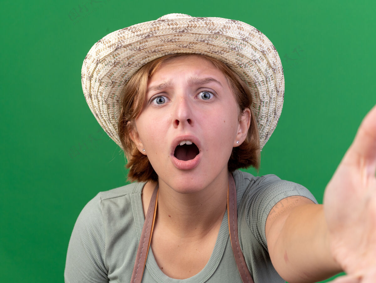 年轻焦急的年轻斯拉夫女园丁戴着园艺帽看着摄像机假装拿着摄像机在草地上焦虑女性园艺