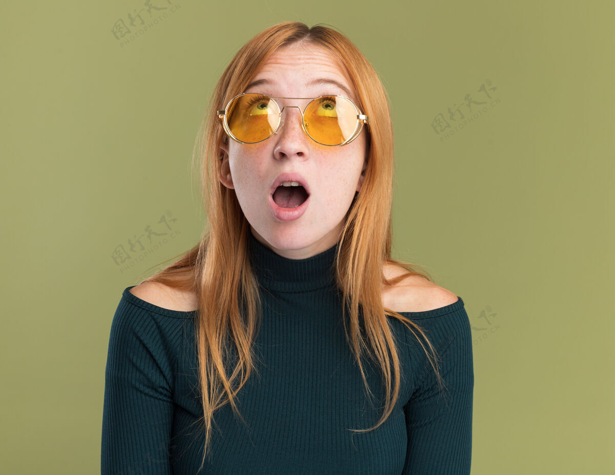 年轻一个戴着太阳镜满脸雀斑的年轻红发姜黄色女孩惊讶地看着橄榄绿眼镜红发惊喜