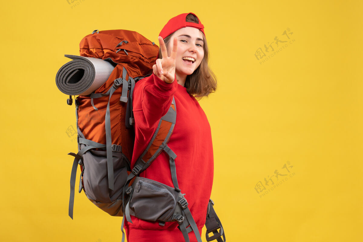 人正面是快乐的女旅行者 背着背包 打着胜利的手势帽子成人快乐
