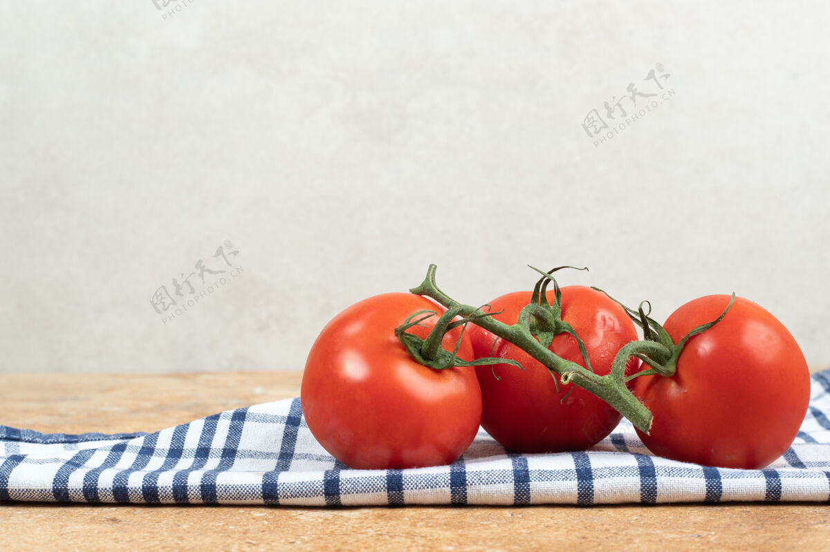 生的桌布上放着一堆新鲜的红西红柿和绿茎素食簇果汁