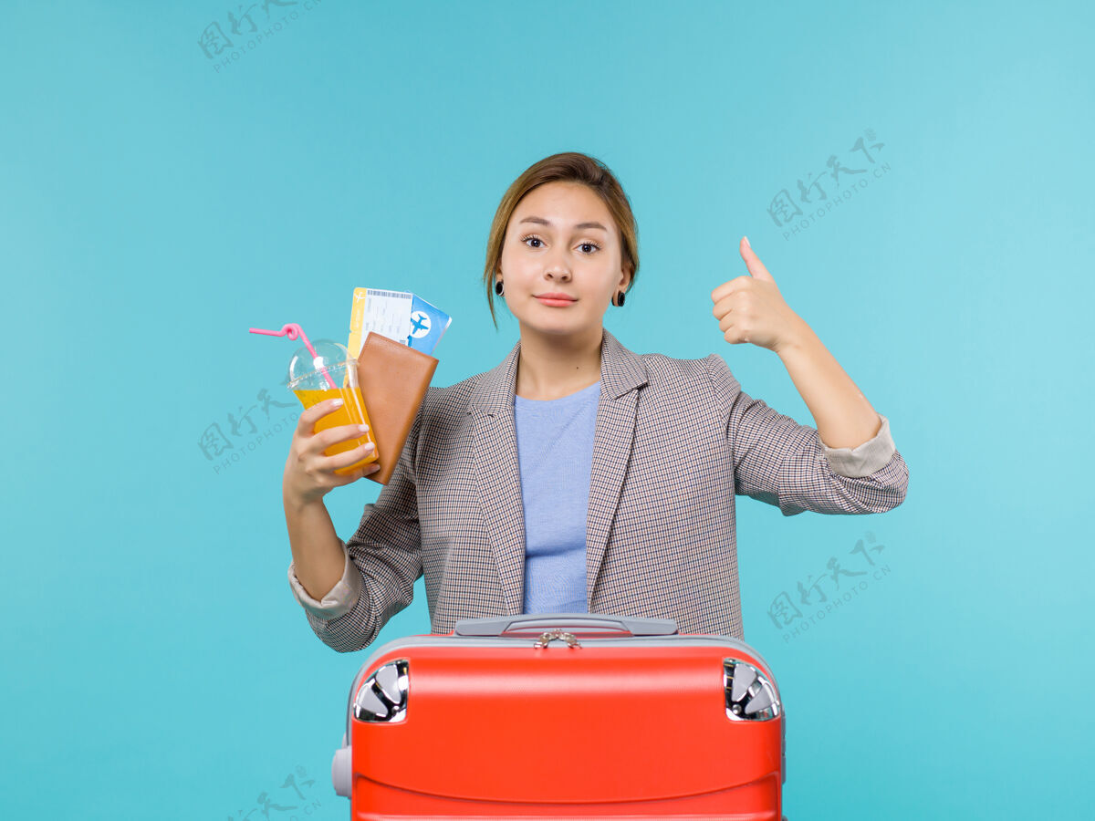 成人正面图：度假中的女性手持新鲜饮料和蓝色背景的机票出海度假旅行肖像欢呼风景