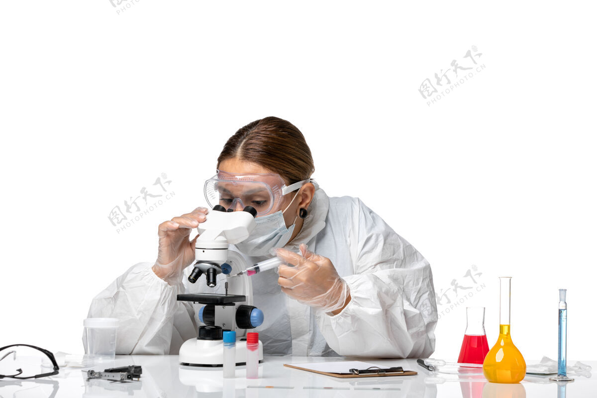 防护前视图：女医生穿着防护服 戴着口罩 用显微镜观察一种白色背景的冠状病毒大流行的健康冠状病毒使用视图大流行