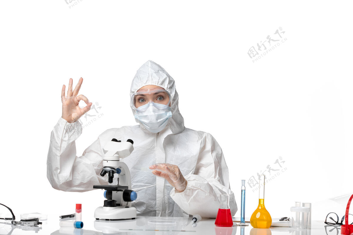 病毒正面图：女医生穿着防护服 戴着口罩 因为在白色办公桌上用显微镜观察病毒大流行 溅起病毒女医生药品视图