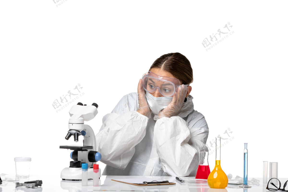 视图正面图女医生穿着防护服 戴着口罩 在显微镜上看白色背景的冠状病毒大流行的健康冠状病毒大流行药品防护