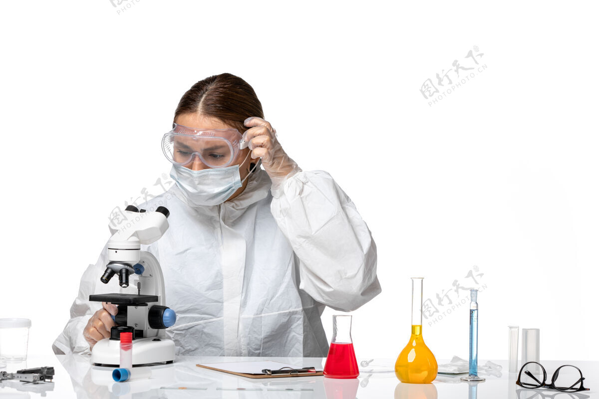 医疗前视图：女医生穿着防护服 戴着口罩 用显微镜观察一个白色背景的健康大流行病毒冠状病毒视图显微镜医生