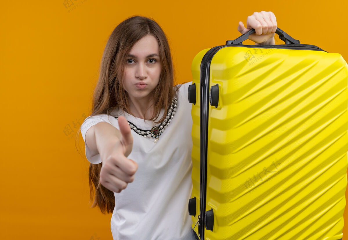 女孩自信的年轻旅行家女孩举起手提箱 在孤立的橙色空间竖起大拇指信心展示手提箱