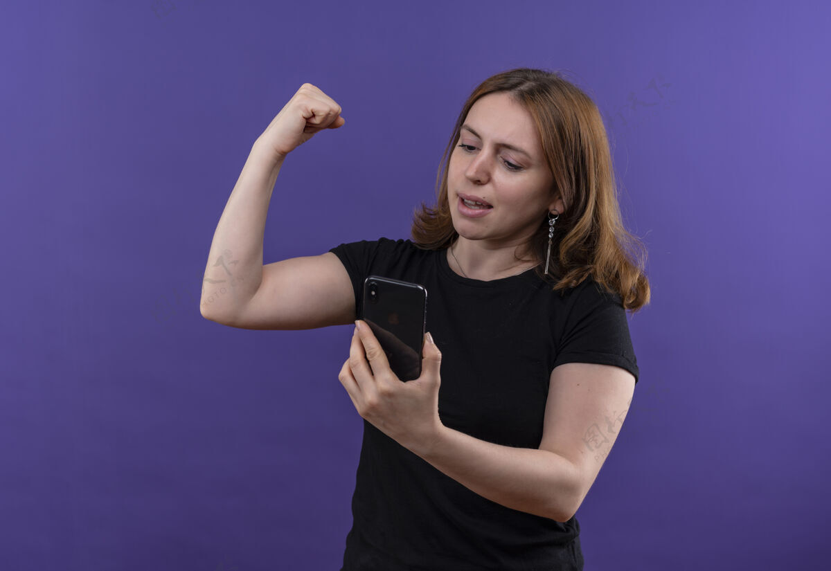 女人自信的年轻随意的女人拿着手机 做着强烈的手势 看着手机在孤立的紫色空间里复制空间电话手势手机