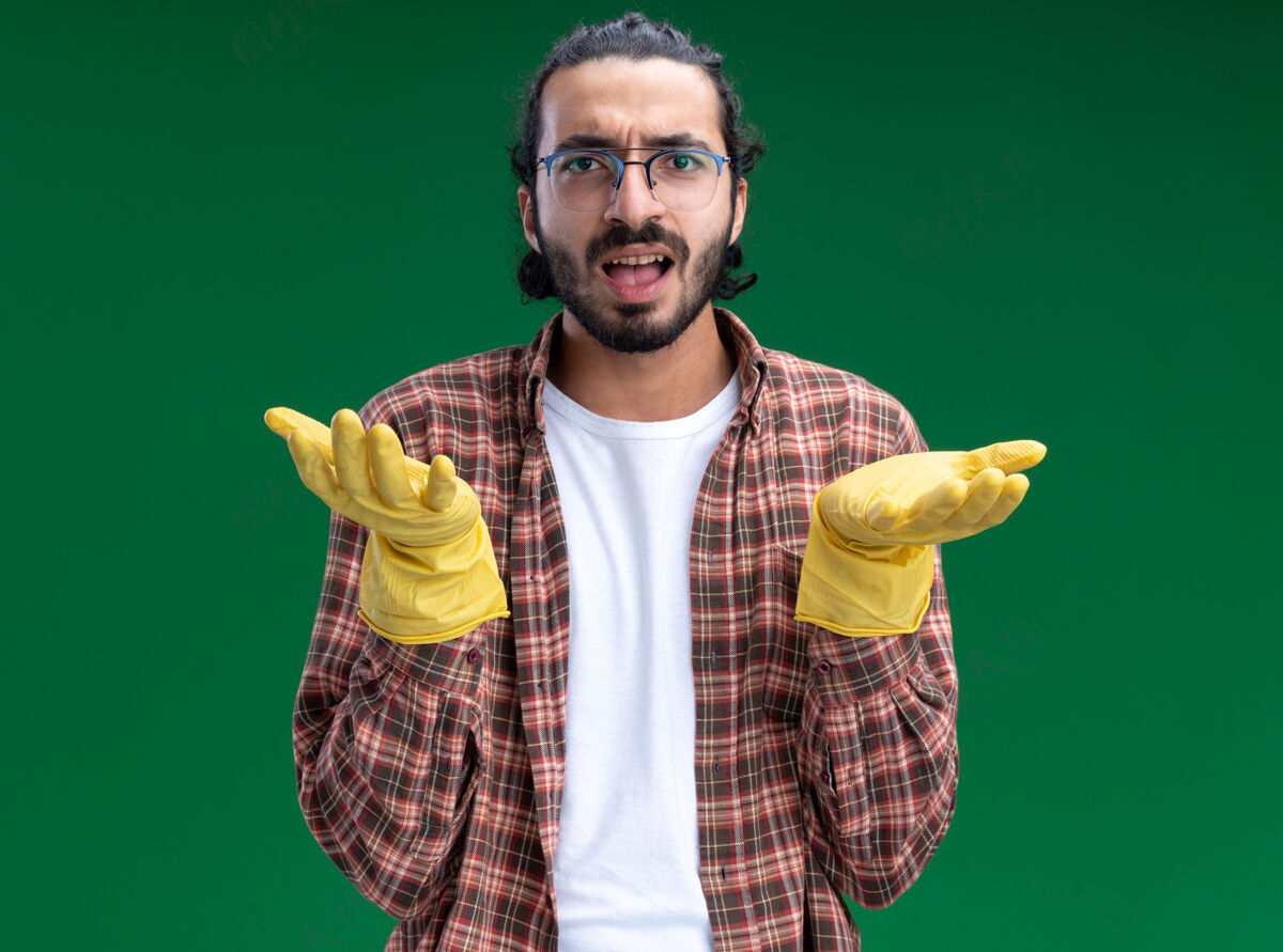 脸困惑的年轻帅气的清洁工穿着t恤和手套摊开双手隔离在绿色的墙上穿着男人手