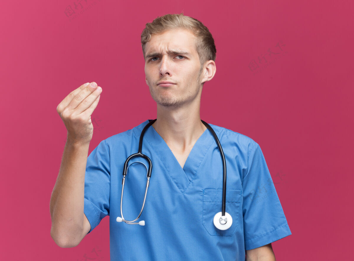 表演悲伤的年轻男医生穿着医生制服 听诊器显示提示手势隔离在粉红色的墙上公民制服人