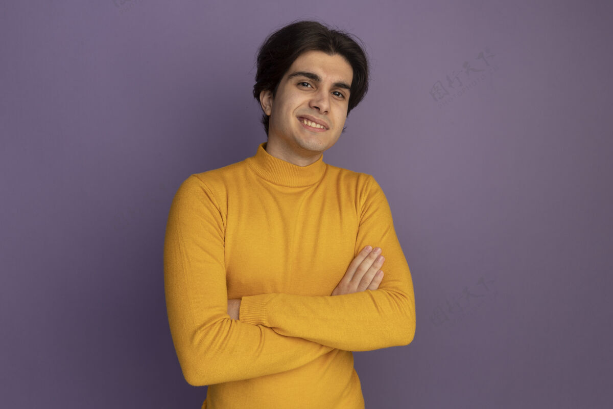 站着微笑的年轻帅哥穿着黄色高领毛衣双手交叉隔离在紫色的墙上 留着复制空间高领毛衣姿势手