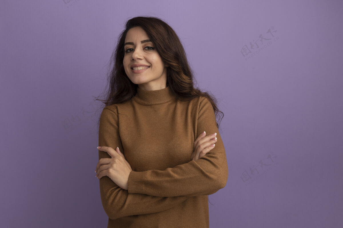 感觉微笑着看着前面年轻漂亮的女孩穿着棕色高领毛衣双手交叉隔离在紫色的墙上与复制空间公民穿着微笑