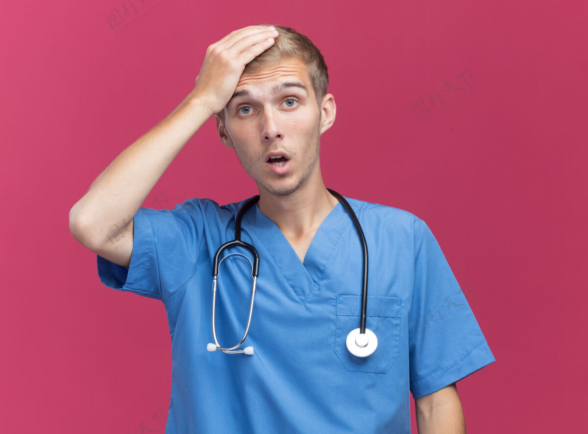 人被吓坏了的年轻男医生穿着医生制服 手放在头上 手被隔离在粉红色的墙上公民人听诊器