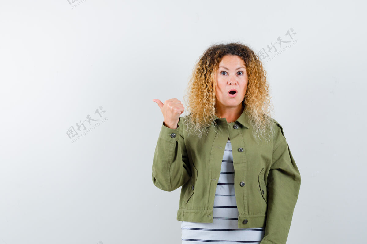 人一个金发卷曲的女人 穿着绿色夹克 用拇指指着一边 很好奇地看着前方微笑指着卷发