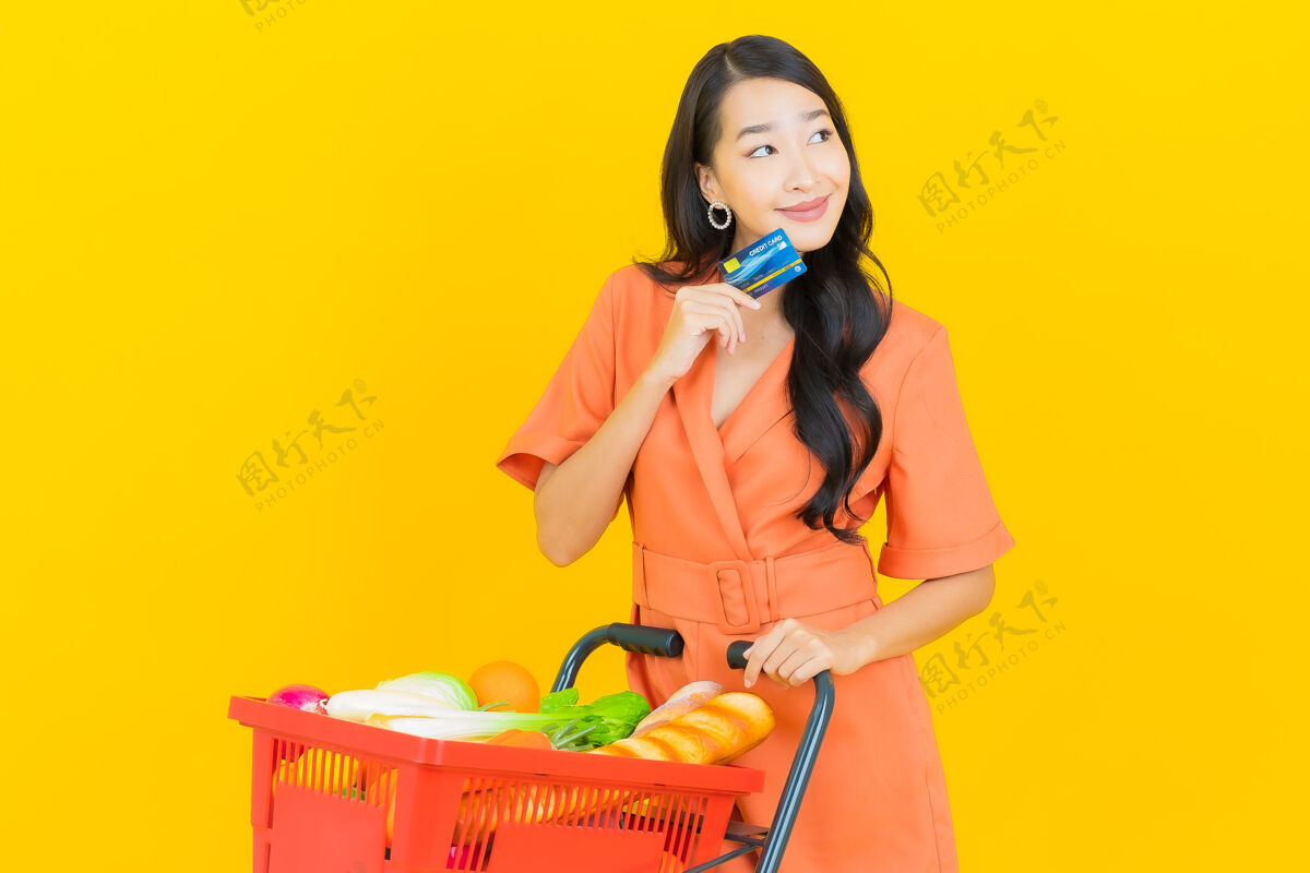 年轻肖像美丽的亚洲年轻女子微笑着从黄色超市购物篮享受购买买家