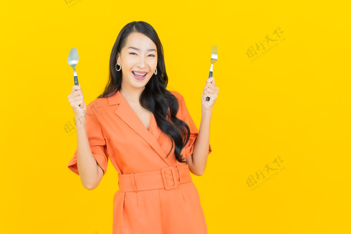 餐桌肖像美丽的亚洲年轻女子微笑着用勺子和叉子在黄色女人叉子餐具