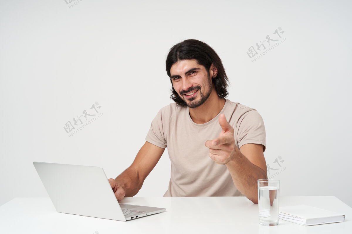 男性开朗的家伙 快乐的商人 黑头发和胡须办公室概念坐在工作场所在笔记本电脑上工作 隔着白墙服装人工作场所