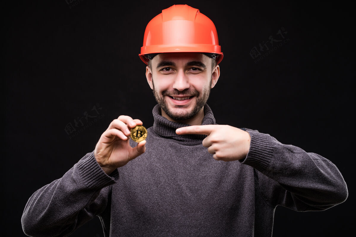 银行英俊的年轻男子矿工在保护帽檐上指出比特币上孤立的黑色商业手人