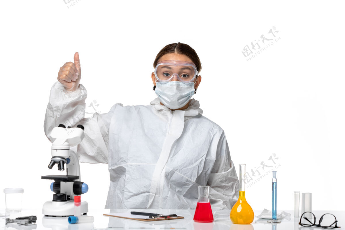 专业正面图：穿着防护服 戴着面罩的女医生坐在白色背景病毒冠状病毒上摆姿势——健康大流行医学病毒医生