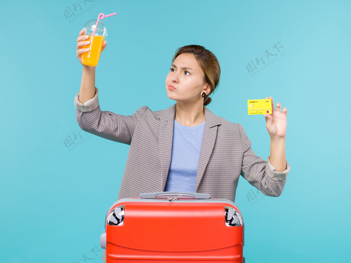 桌子前景：度假中的女性拿着新鲜果汁和银行卡在蓝色办公桌上海上旅行度假飞机旅行假期女人银行
