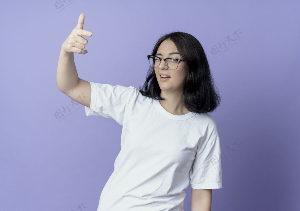自信自信的年轻漂亮的白人女孩戴着眼镜 对着镜头眨眼 做着的手势 背景是紫色的 有复制空间年轻女孩