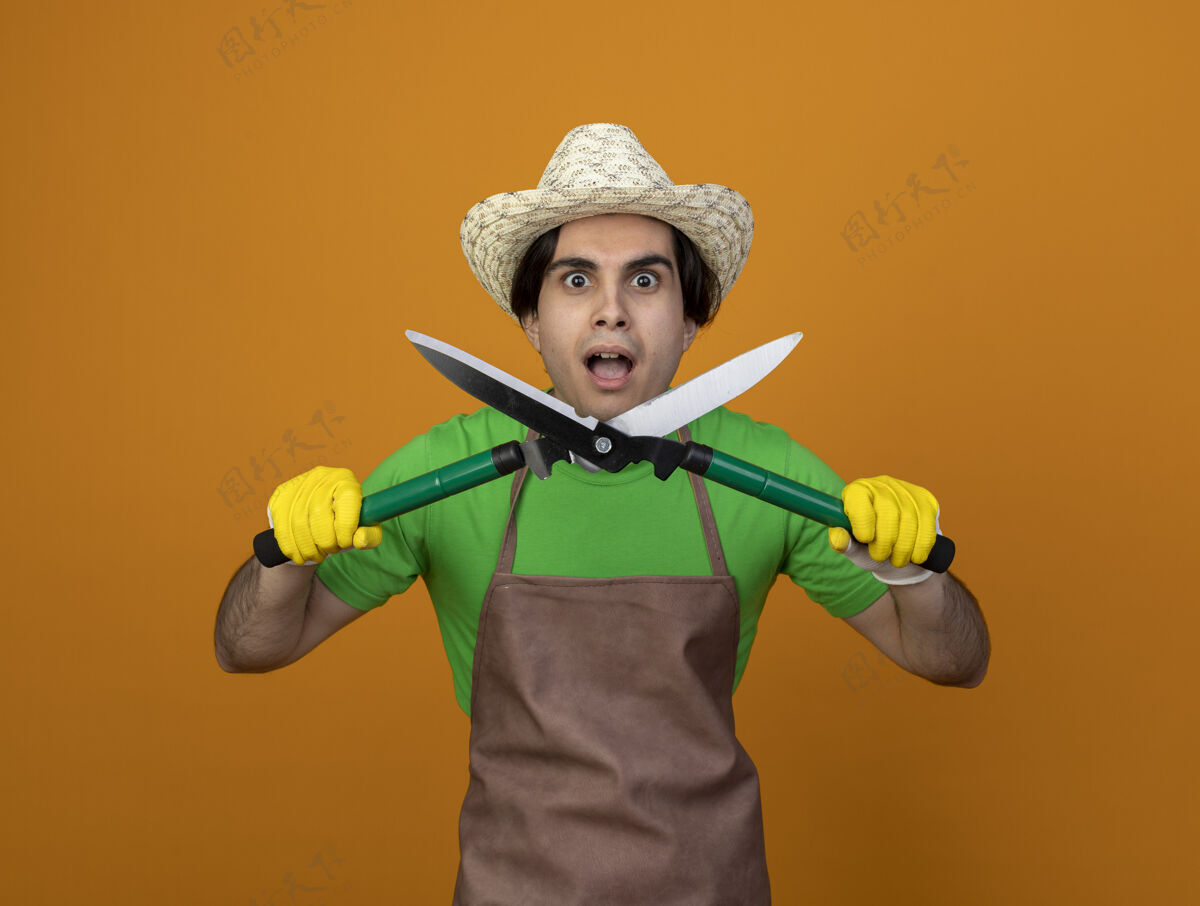 男人穿着制服的年轻男园丁惊讶地戴着园艺帽 戴着手套拿着剪刀男人抱着穿