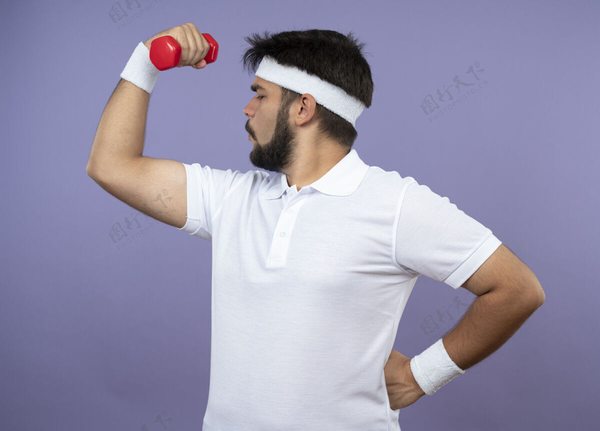 哑铃年轻的运动型男子站在侧视图戴着头带和腕带锻炼哑铃把手放在臀部男人头带运动