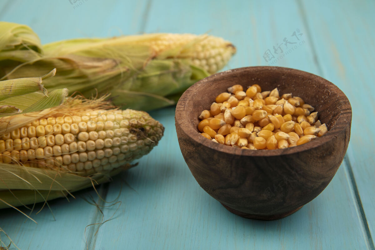 木材蓝色木桌上的木碗上有头发和玉米粒的有机玉米俯视图蓝色新鲜食物