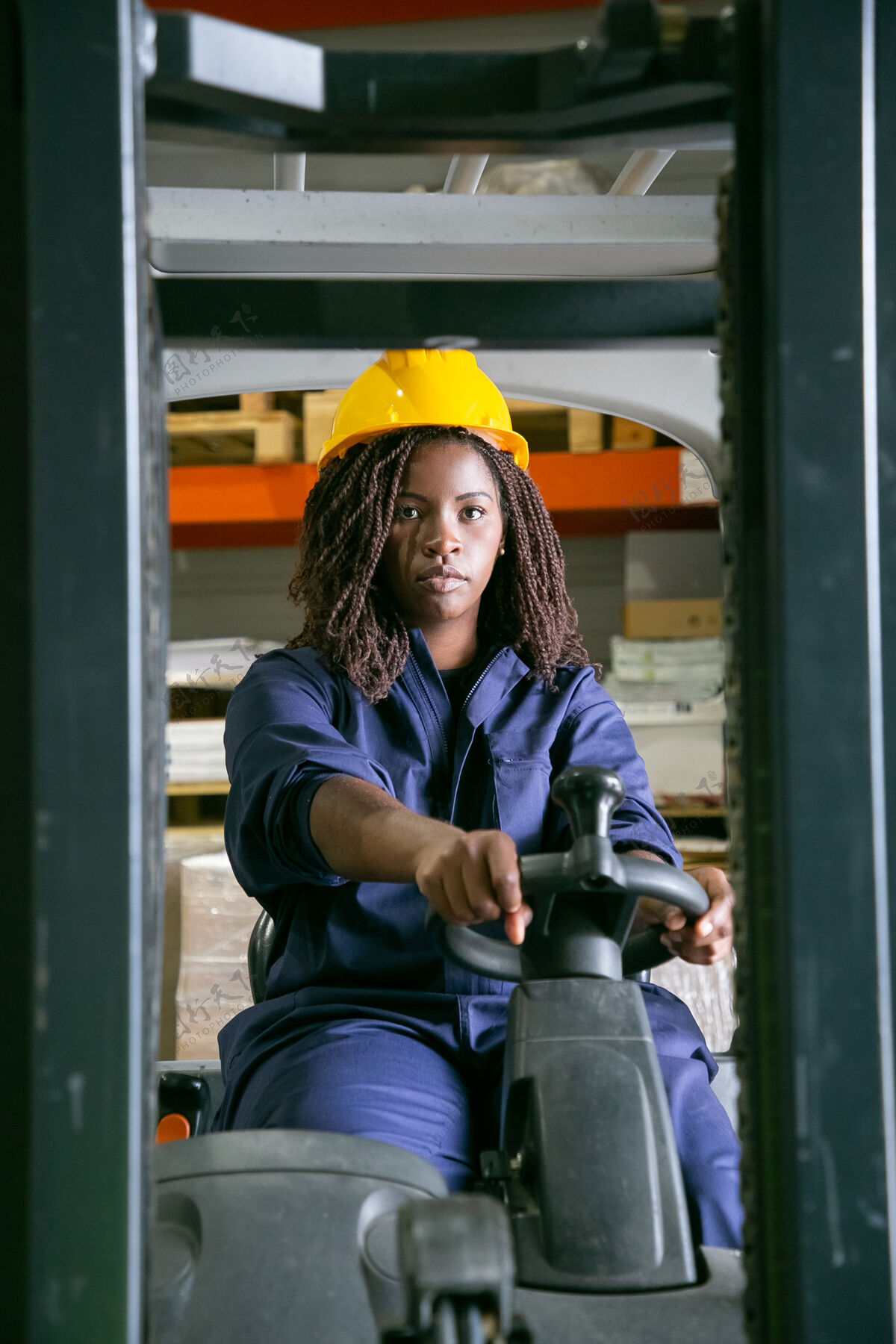 年轻人严肃的女仓库工人戴着安全帽操作叉车 看着前方成人工厂驾驶