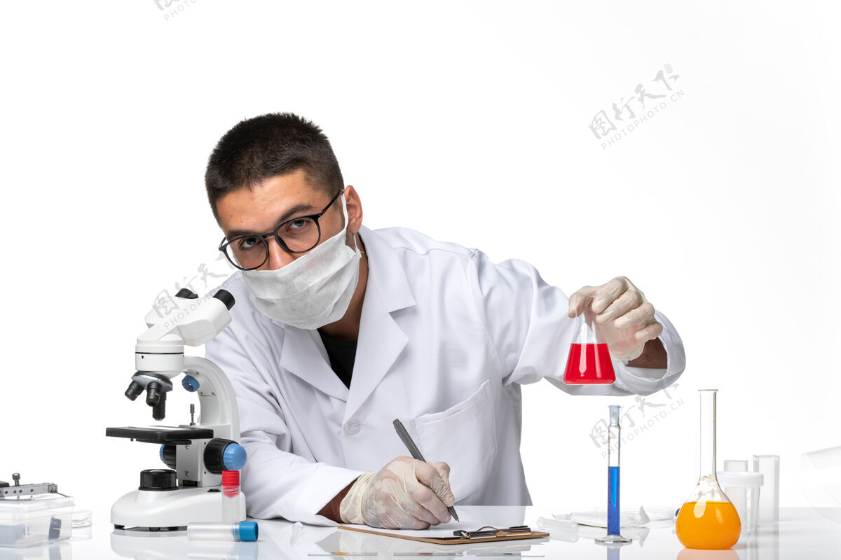 面罩正面图：男医生穿着白色医疗服 戴着面罩 白色桌子上放着红色溶液专业人员工作服红色