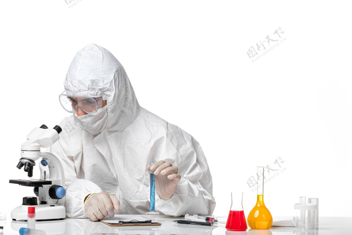解决方案正面图：男医生穿着防护服 戴着面罩 因为在空白处有蓝色溶液的瓶子蓝病毒西装