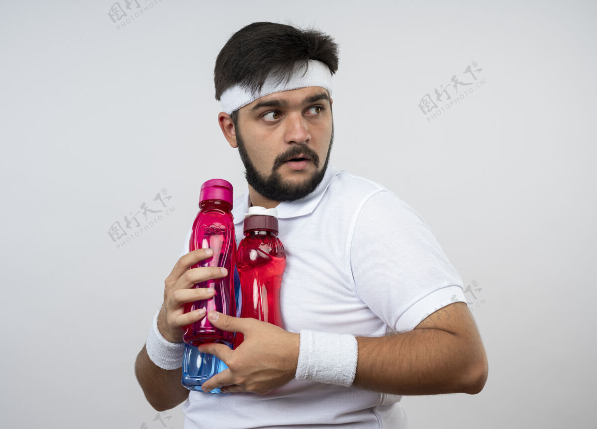 头带贪婪的年轻人戴着头带和腕带拿着水瓶孤立在白墙上男人运动瓶子