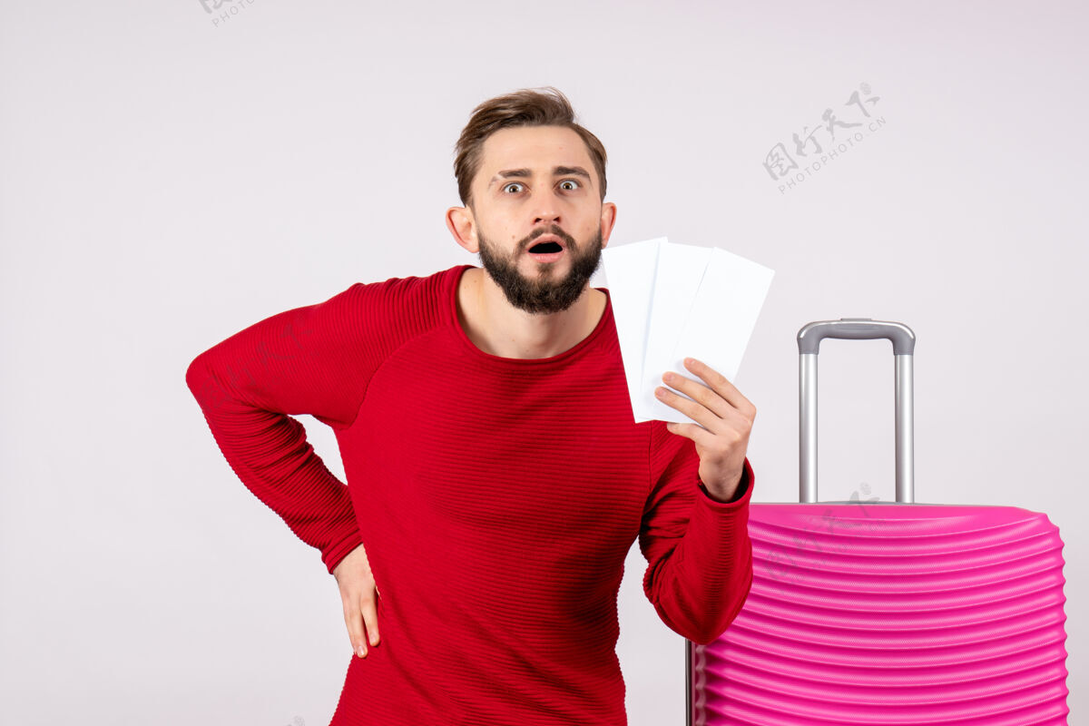 年轻男性正面图：年轻男性 带着粉色包 手持飞机票 在白墙上航行 飞行旅行 度假 旅游者的情感照片机票游客成人