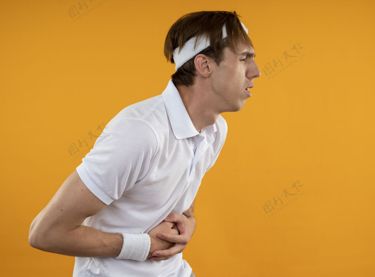 年轻一个戴着头带和腕带的年轻的运动型的家伙把胃隔离在黄色的墙上头带家伙肚子